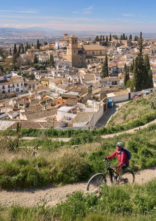 Photo for Nice active senior woman cycling with her electric mountain bike in Granada below the world heritage site of Alhambra, Granada, Andalusia,  Spain, - Royalty Free Image