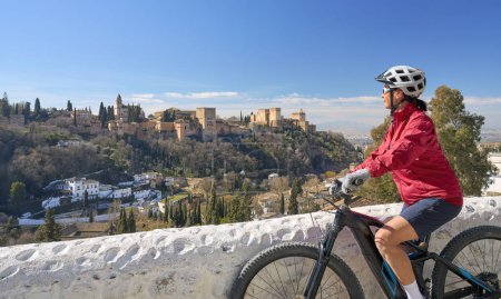 Nette aktive Seniorin fährt mit ihrem Elektro-Mountainbike in Granada unterhalb des Weltkulturerbes Alhambra, Granada, Andalusien, Spanien,