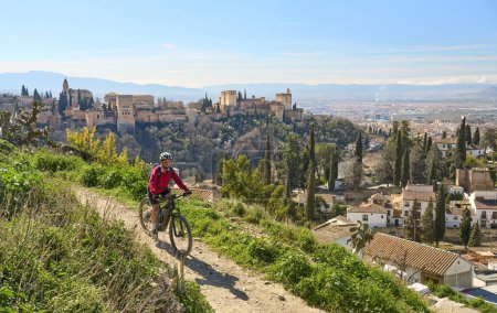 Foto de Bonita mujer mayor activa en bicicleta con su bicicleta de montaña eléctrica en Granada por debajo del Patrimonio de la Humanidad de Alhambra, Granada, Andalucía, España, - Imagen libre de derechos