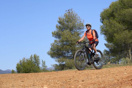 Photo for Nice, active senior woman riding her electric mountain bike in the pine tree forests near Granada, Andalusia, Spain - Royalty Free Image