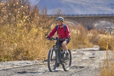 Téléchargez les photos : Belle femme âgée active avec son vélo de montagne électrique lors d'un tour de piste dans le désert de Tabernas près d'Almeria, Andlusia, Espagne - en image libre de droit