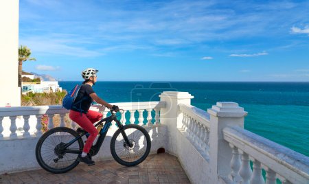 Photo for Nice senior woman cycling with her electric mountain bike at the Costa Blanca coastline near Nerja, Andalusia, Spain - Royalty Free Image