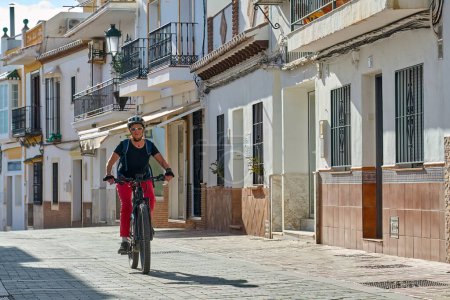 Téléchargez les photos : Belle femme âgée vélo avec son vélo de montagne électrique dans le pittoresque village blanc de Frigiliana près de Nerja, Andalousie, Espagne - en image libre de droit