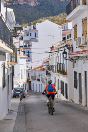 agradable mujer mayor en bicicleta con su bicicleta de montaña eléctrica en el pintoresco pueblo blanco de Frigiliana cerca de Nerja, Andalucía, España