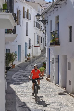 agradable mujer mayor en bicicleta con su bicicleta de montaña eléctrica en el pintoresco pueblo blanco de Frigiliana cerca de Nerja, Andalucía, España