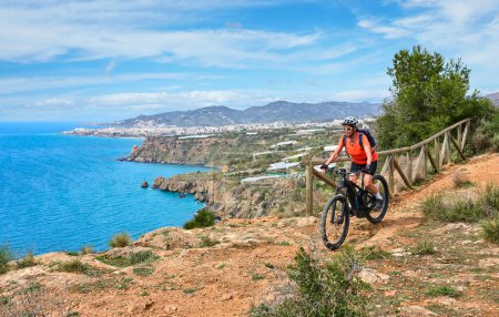 Photo for Nice senior woman cycling with her electric mountain bike at the Costa Blanca coastline near Nerja, Andalusia, Spain - Royalty Free Image