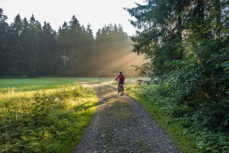 mujer mayor, montando una bicicleta de montaña eléctrica en una mañana atmosférica al amanecer