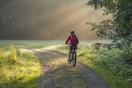 Photo for Senior woman, riding an electrical mountainbike on an atmosperic morning at sunrise - Royalty Free Image