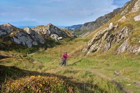 Photo for Nice senior woman on mountain bike, cycling in sunset on the cliffs of Sheeps Head, County Cork, in the southnwestern part of the Republic of Ireland - Royalty Free Image