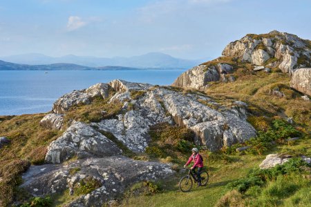 Photo for Nice senior woman on mountain bike, cycling in sunset on the cliffs of Sheeps Head, County Cork, in the southnwestern part of the Republic of Ireland - Royalty Free Image