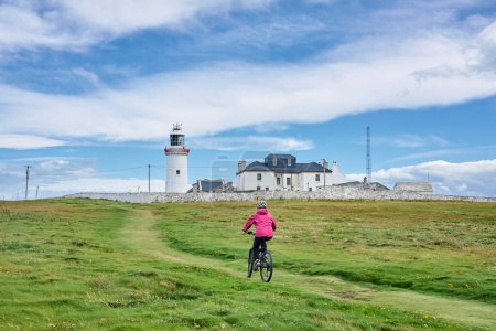 Photo for Nice senior woman on mountain bike, cyclingat Dunmore Head Lighthouse near Kilballyowen , County Limerick in the southwestern part of the Republik of Ireland - Royalty Free Image