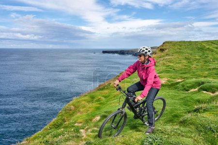 Foto de Agradable mujer mayor en bicicleta de montaña, ciclismo en los acantilados de Dunmore Head cerca de Kilballyowen, Condado de Limerick en la parte suroeste de la República de Irlanda - Imagen libre de derechos