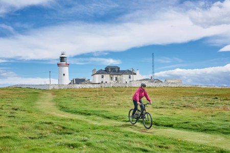Photo for Nice senior woman on mountain bike, cyclingat Dunmore Head Lighthouse near Kilballyowen , County Limerick in the southwestern part of the Republik of Ireland - Royalty Free Image