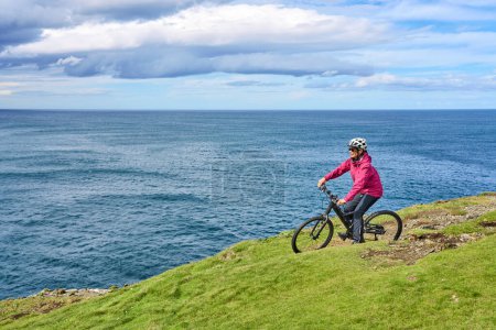 Foto de Agradable mujer mayor en bicicleta de montaña, ciclismo en los acantilados de Dunmore Head cerca de Kilballyowen, Condado de Limerick en la parte suroeste de la República de Irlanda - Imagen libre de derechos