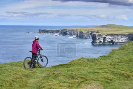 Téléchargez les photos : Belle femme âgée en VTT, faisant du vélo sur les falaises de Dunmore Head près de Kilballyowen, comté de Limerick dans la partie sud-ouest de la Republik d'Irlande - en image libre de droit