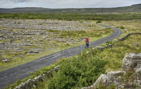 agradable mujer mayor en bicicleta de montaña, ciclismo en la áspera zona kárstica de Burren cerca de Ballyvaughan, Condado de Clare en la parte occidental de la República de Irlanda