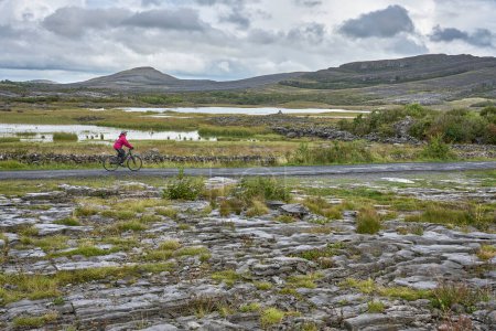Foto de Agradable mujer mayor en bicicleta de montaña, ciclismo en la áspera zona kárstica de Burren cerca de Ballyvaughan, Condado de Clare en la parte occidental de la República de Irlanda - Imagen libre de derechos