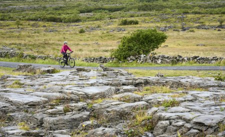 nice senior woman on mountain bike, cycling in the rough karst area of Burren near Ballyvaughan, County Clare in the western part of the Republic of Ireland