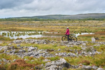 Photo for Nice senior woman on mountain bike, cycling in the rough karst area of Burren near Ballyvaughan, County Clare in the western part of the Republic of Ireland - Royalty Free Image