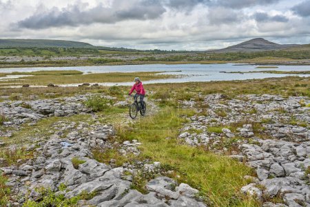 nice senior woman on mountain bike, cycling in the rough karst area of Burren near Ballyvaughan, County Clare in the western part of the Republic of Ireland