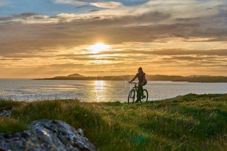 Photo for Nice senior woman on mountain bike, cycling in sunset at the golden sand beach of Sillerna, Grallagh, County Galway, in the western part of the Republic of Ireland - Royalty Free Image