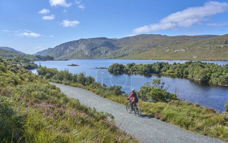 Photo for Nice senior woman on mountain bike, cycling at Lough Beagh in the Glenveagh National park, near Churchill, Donegal, northern Republic of Ireland - Royalty Free Image