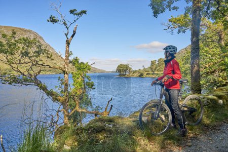 Foto de Agradable mujer mayor en bicicleta de montaña, ciclismo en Lough Beagh en el Parque Nacional Glenveagh, cerca de Churchill, Donegal, norte de la República de Irlanda - Imagen libre de derechos