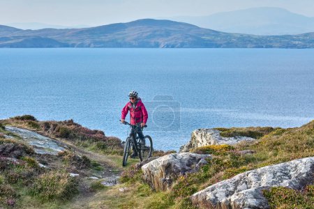 Téléchargez les photos : Belle femme âgée en VTT, vélo au coucher du soleil sur les falaises de Sheeps Head, comté de Cork, dans le sud-ouest de la République d'Irlande - en image libre de droit
