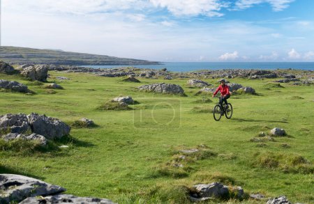 nice senior woman on mountain bike, cycling in the rough karst area of Burren near Ballyvaughan, County Clare in the western part of thr Republic of Ireland