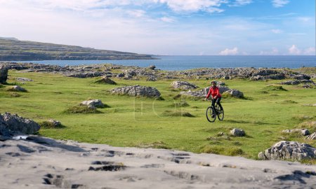 Photo for Nice senior woman on mountain bike, cycling in the rough karst area of Burren near Ballyvaughan, County Clare in the western part of thr Republic of Ireland - Royalty Free Image