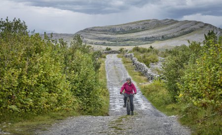 nice senior woman on mountain bike, cycling in the rough karst area of Burren near Ballyvaughan, County Clare in the western part of thr Republic of Ireland