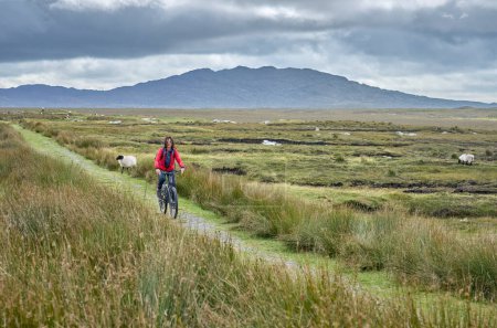 Photo for Nice senior woman on mountain bike, cycling bog Area near Derrycunlagh, County Galway, in  the western part of the Republic of Ireland - Royalty Free Image