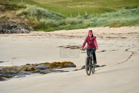 Foto de Agradable mujer mayor en bicicleta de montaña, ciclismo en la puesta de sol en la playa de arena dorada de Sillerna, Grallagh, Condado de Galway, en la parte occidental de la República de Irlanda - Imagen libre de derechos