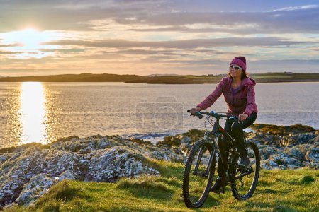 Photo for Nice senior woman on mountain bike, cycling in sunset at the golden sand beach of Sillerna, Grallagh, County Galway, in the western part of the Republic of Ireland - Royalty Free Image