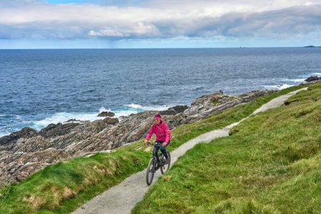 Téléchargez les photos : Belle femme âgée en VTT, faisant du vélo sur les falaises de Malin Head, le point le plus au nord de l'Irlande - en image libre de droit