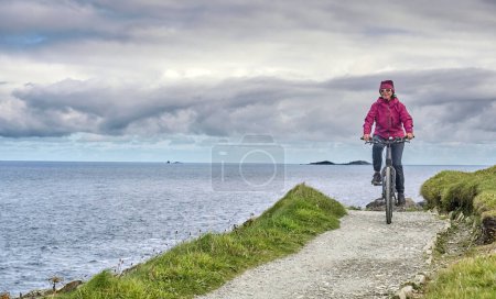 Foto de Agradable mujer mayor en bicicleta de montaña, ciclismo en los acantilados de Malin Head, el punto más septentrional de Irlanda - Imagen libre de derechos