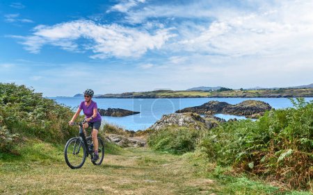 Photo for Nice senior woman on mountain bike, cycling on the cliffs of Malin Head, the northern most point of Ireland - Royalty Free Image