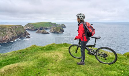 Téléchargez les photos : Belle femme âgée en VTT, faisant du vélo sur les falaises de Malin Head, le point le plus au nord de l'Irlande - en image libre de droit