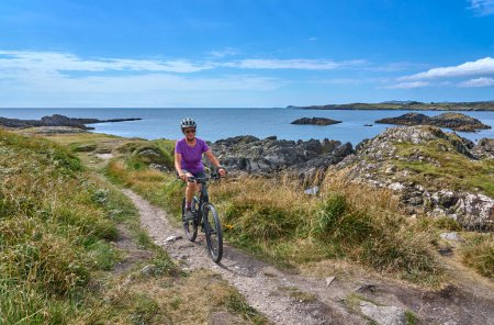 Photo for Nice senior woman on mountain bike, cycling on the cliffs of Tooremore, County Cork in southwestern Ireland - Royalty Free Image