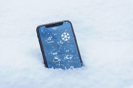 Téléchargez les photos : Phone with the current temperature in Celsius and with the weather forecast for the coming days. Modern app interface. The phone sank into the snow - en image libre de droit