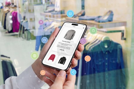 Woman's hands hold a smartphone with shopping app surrounded by shopping icons, while a boutique showcases clothes in the background