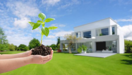 Photo for Hand hold seedling with modern, energy-efficient home in background, embracing eco-design, reducing SO2 emissions for a sustainable, green lifestyle concept - Royalty Free Image