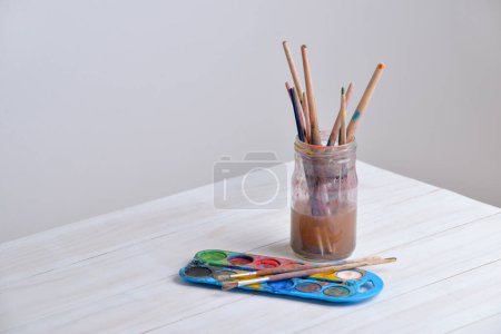Foto de Tarro con pinceles y acuarelas sobre mesa de madera. Ideal para proyectos creativos o temas artísticos - Imagen libre de derechos