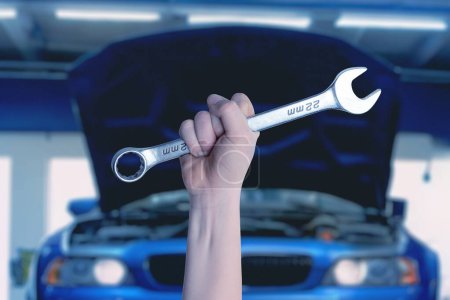 Photo for Wrench in hand in front of a blue car with an open engine compartment. Ready for service and maintenance. Professional automotive concept - Royalty Free Image