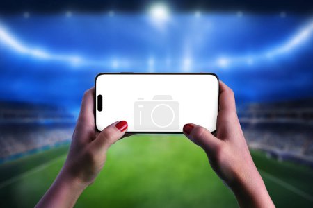 Teléfono móvil sostenido horizontalmente en las manos en un estadio de fútbol, perfecto para diseños temáticos deportivos y el concepto de tecnología