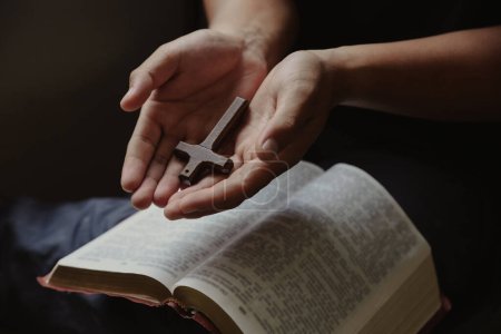 Foto de La cruz descansó en la mano del joven mientras leía y estudiaba la Biblia, concepto de fe para Dios. - Imagen libre de derechos