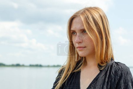 beautiful girl in a black dress on the background of the river, sea with blue sky and clouds close-up