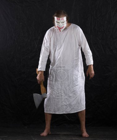 Photo for Maniac in a hockey mask in a medical gown on a black background - Royalty Free Image