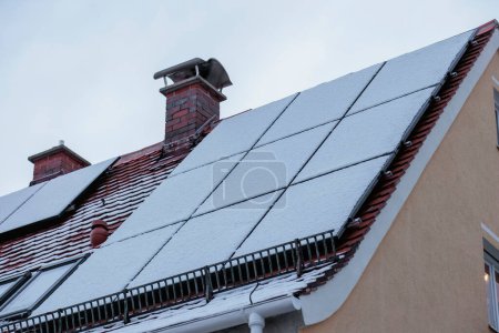 Téléchargez les photos : Les modules photovoltaïques recouverts de neige sur le toit d'une maison ne fournissent pas d'électricité - en image libre de droit