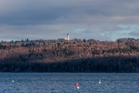 Téléchargez les photos : At the Ammersee the towers of Andechs monastery stand between wintry woods and the cloudy sky - en image libre de droit